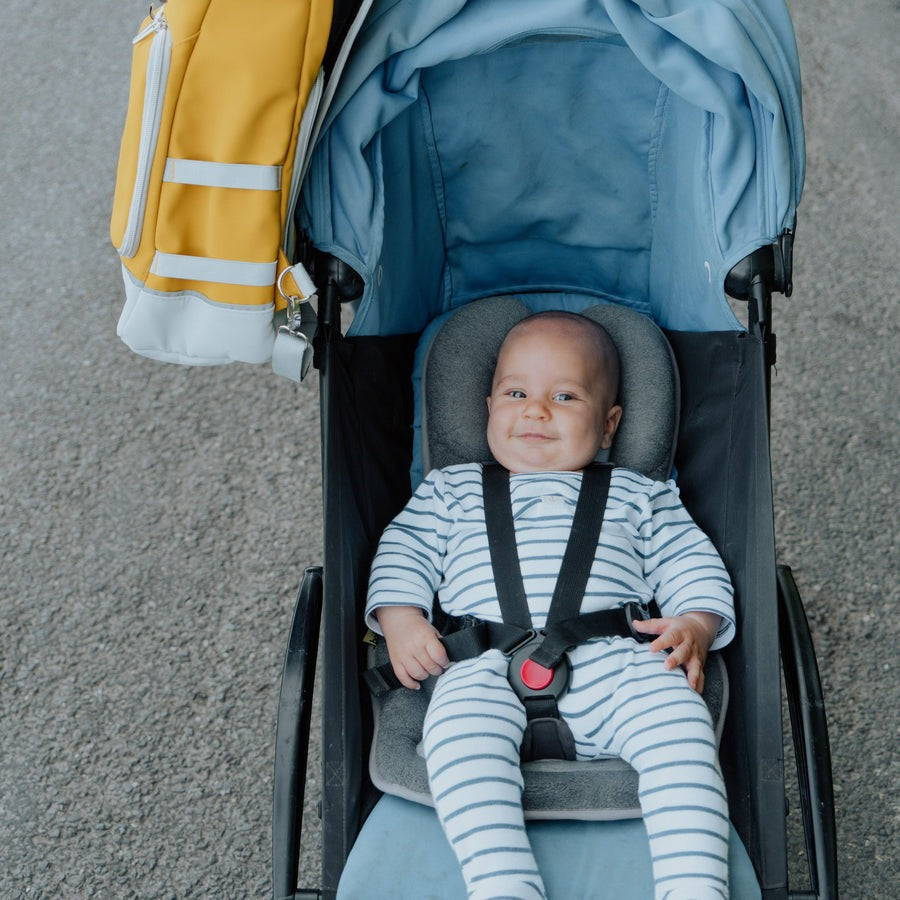 Babymoov Cozymorpho Smokey stroller with smiling baby in a blue canopy and striped onesie secured in harness