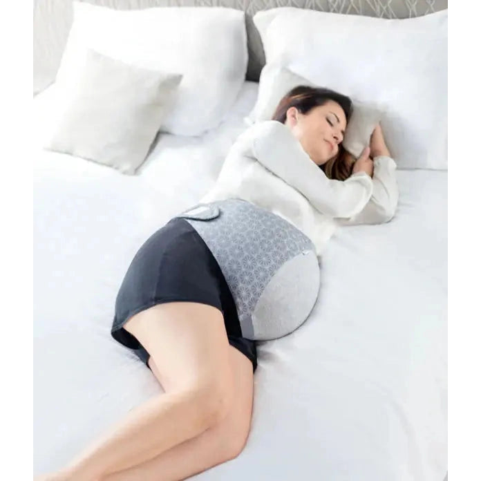 Babymoov Dream Belt Pregnancy Belt Sleep Solution supports a pregnant belly while a woman sleeps on a white bed.