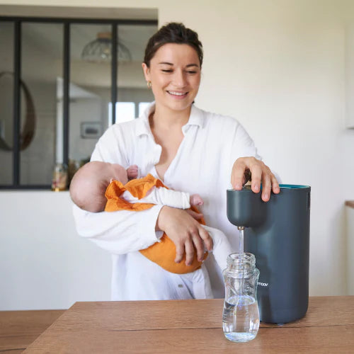 Babymoov Instant Baby Bottle Warmer Milky Now in dark gray with glass water bottle on table