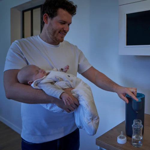 Babymoov Instant Baby Bottle Warmer Milky Now on blue countertop; man holding a baby.