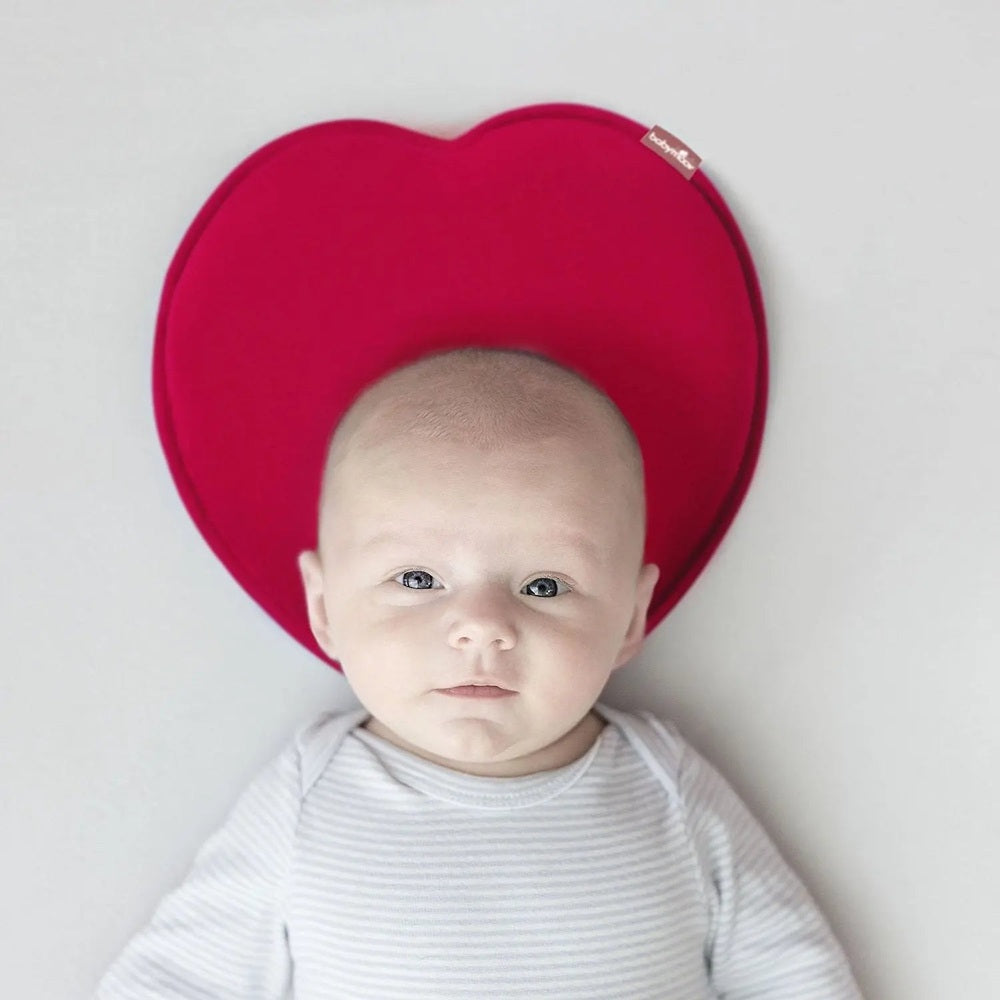 Babymoov Lovenest Pillow red heart-shaped nursing cushion cradling baby’s head as infant rests.