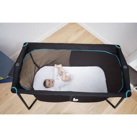 Babymoov Naos travel crib and playard with black fabric and blue trim, baby on white mattress.