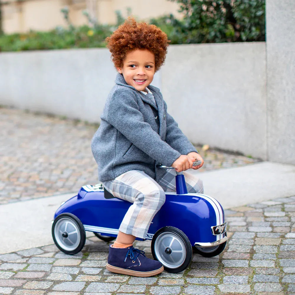 Baghera Ride-On Ford Mustang blue pedal car, a smiling child riding on a cobblestone path.