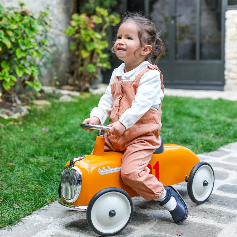 Baghera Ride-On Roaster Camel push-pedal toy car in bright orange, toddler riding along garden path.