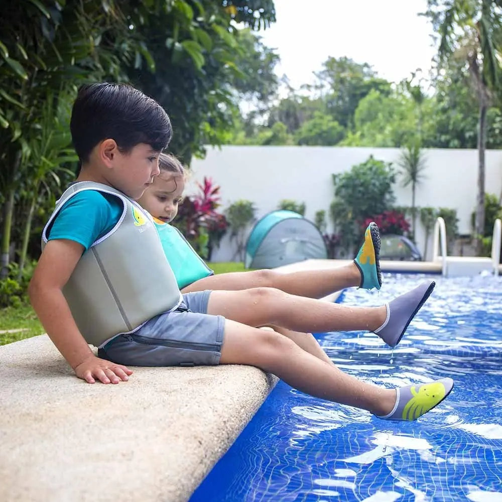 BBLUV Naj Evolutive Neoprene Swim Vest Aqua; two kids sit on pool edge wearing aqua vests, kicking legs into water.