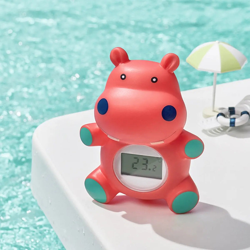 BC Babycare Baby Bath/Room Thermometer in pink hippo shape with teal paws, digital display reads 23.2°C on a poolside table.