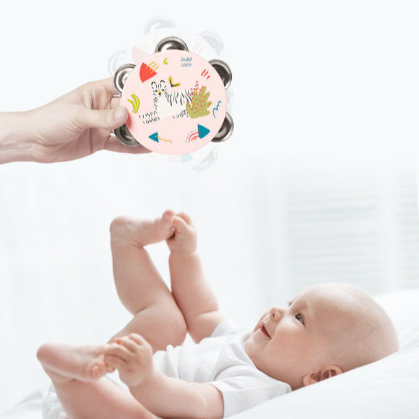 BC Babycare baby tambourine toy; pink printed disc with colorful shapes, held by adult near baby