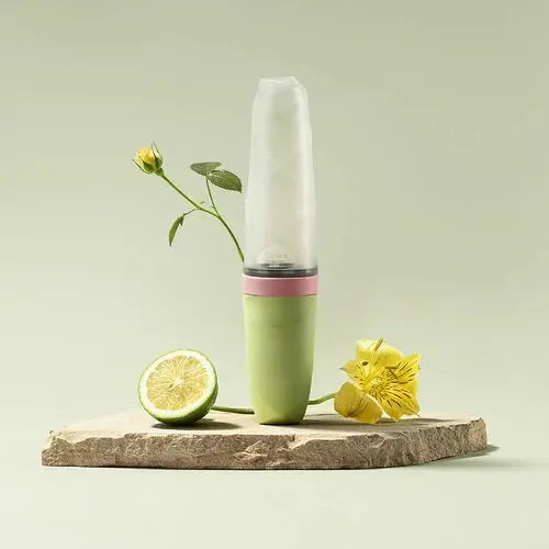 BC Babycare Feeding Spoon Dispenser in pastel green with pink band, standing upright with a transparent cap on a stone slab.