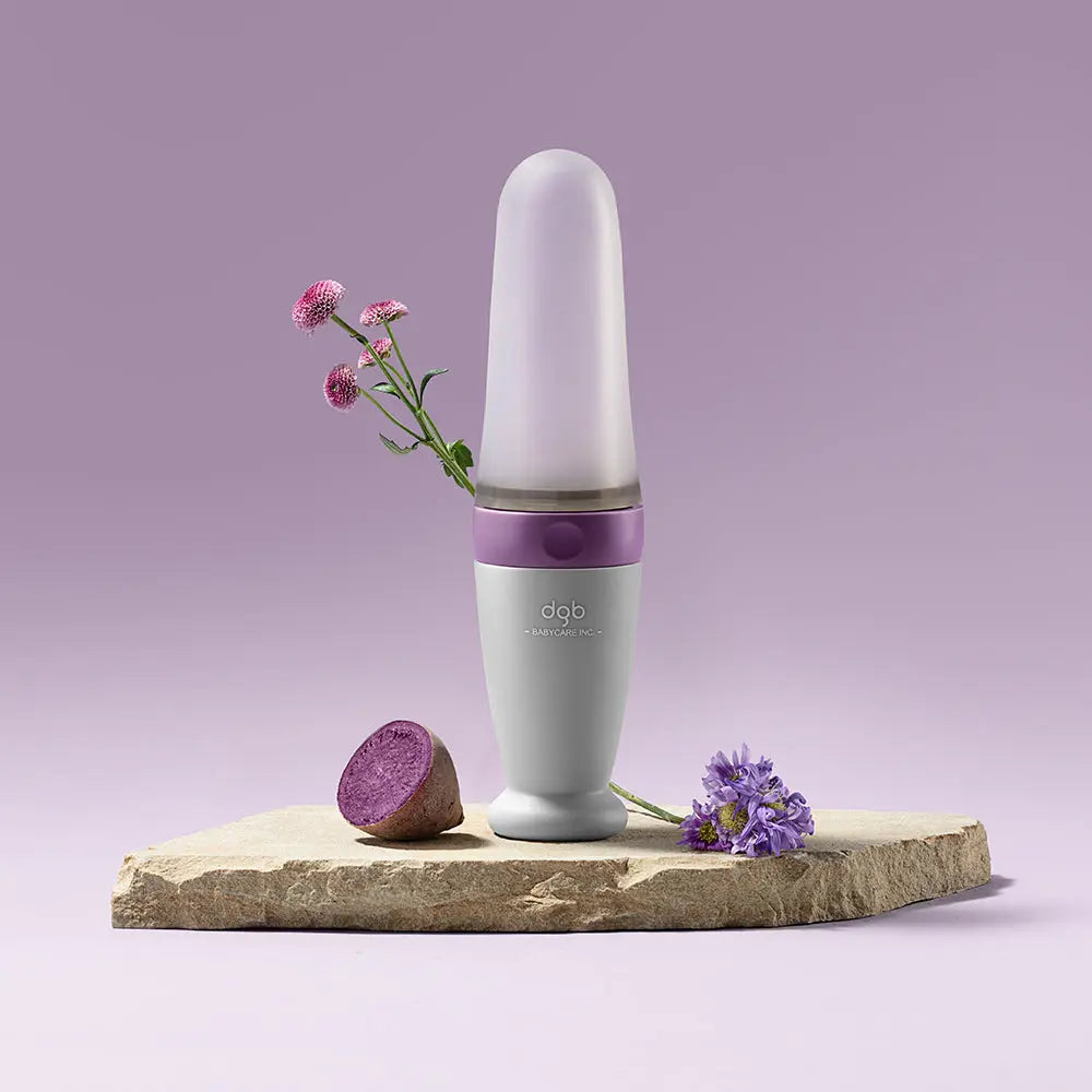 Bc Babycare Feeding Spoon Dispenser standing upright on a stone slab; lilac cap and gray body demonstrate easy spoon dispensing.