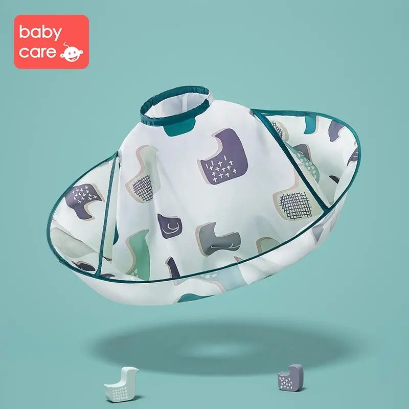 Bc Babycare Haircut Cloak, white cape with teal trim and colorful pattern, shown floating mid‑air for easy grooming.