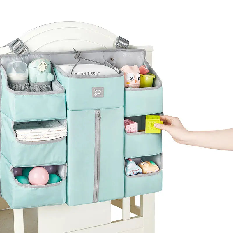 BC Babycare Hanging Storage Bag in mint teal, hanging from a crib rail with multiple pockets storing bottles, toys, and blocks.