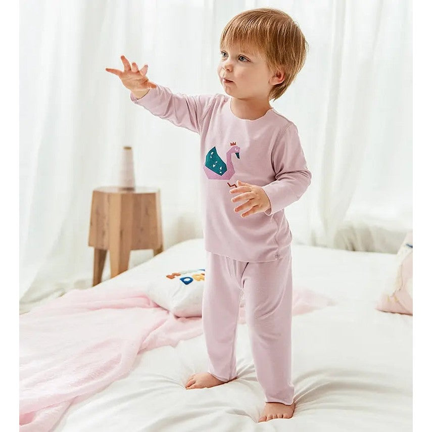 BC Babycare Modal Sleepsuit Pink: toddler in a pink sleepsuit with a swan graphic stands on a bed, reaching forward.
