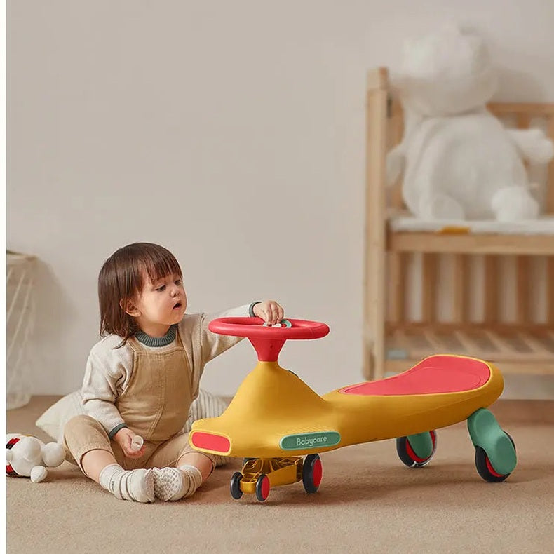 Bc Babycare Nyokiroad Wiggle Car riding toy; yellow body, red seat, green wheels as a child sits and turns the steering wheel.