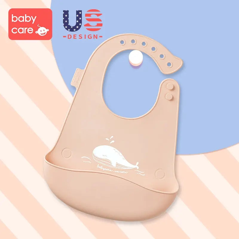 BC Babycare Silicone Adjustable Bib in beige with whale graphic, shown catching spills as a baby wears it.