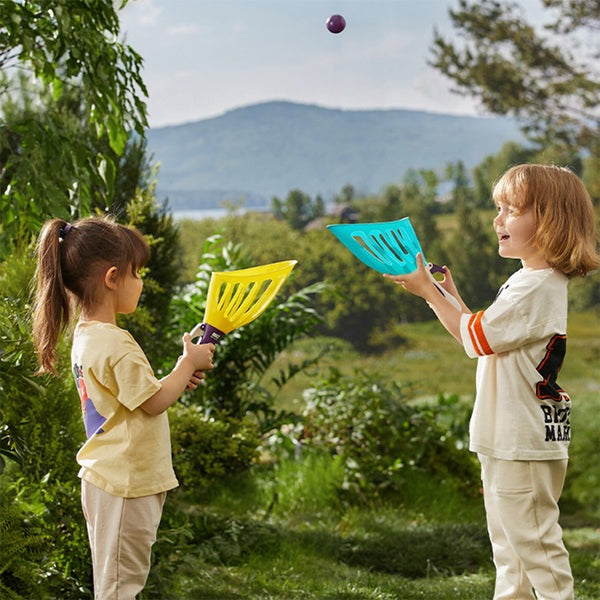 Bc Babycare Toss & Catch Ball Set; two kids outdoors with yellow and blue paddles and a ball