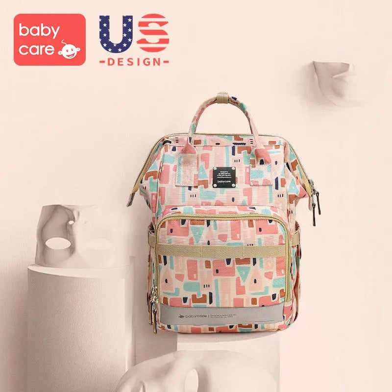 BC Babycare Waterproof Diaper Bag backpack in pastel geometric pattern with beige trim, held by top handle to show multiple pockets