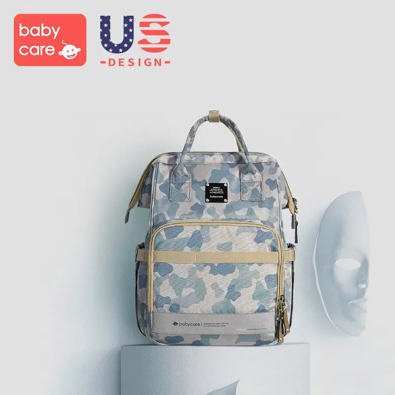 BC Babycare Waterproof Diaper Bag Backpack in camo print with beige straps, shown on a pedestal.