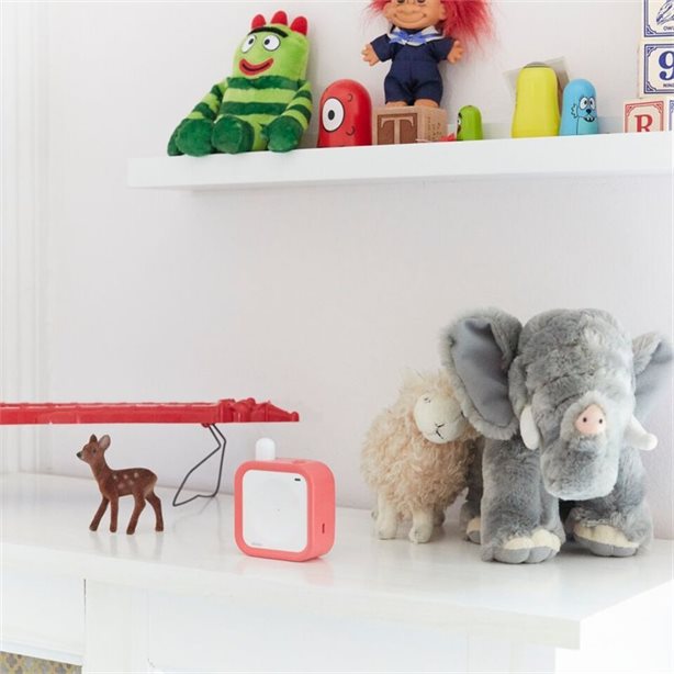 Beaba Minicall Audio Baby Monitor in coral on a white shelf with plush toys