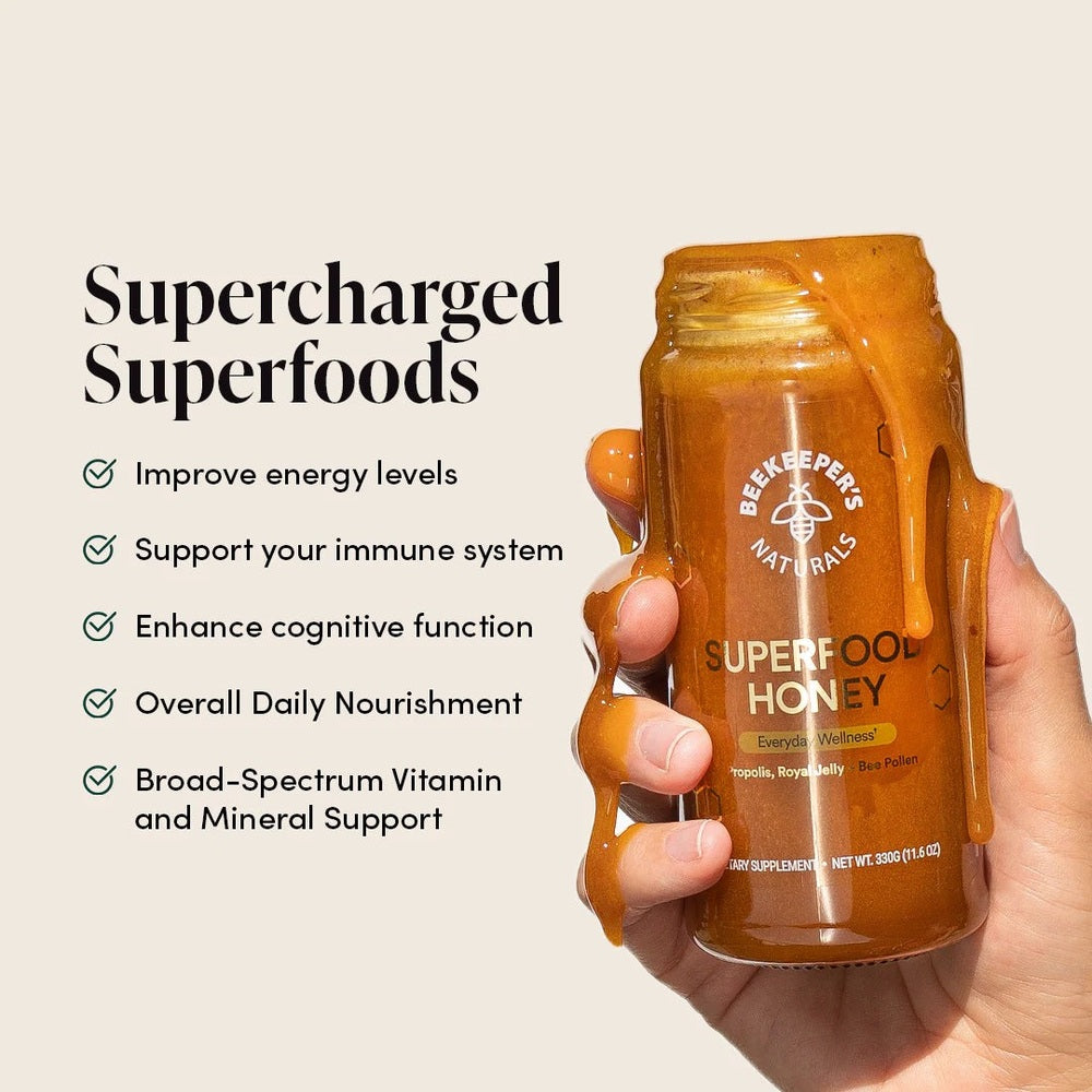 Beekeeper's Naturals Superfood Honey 330g bottle held upright as golden honey drips, illustrating boosted energy and immunity.