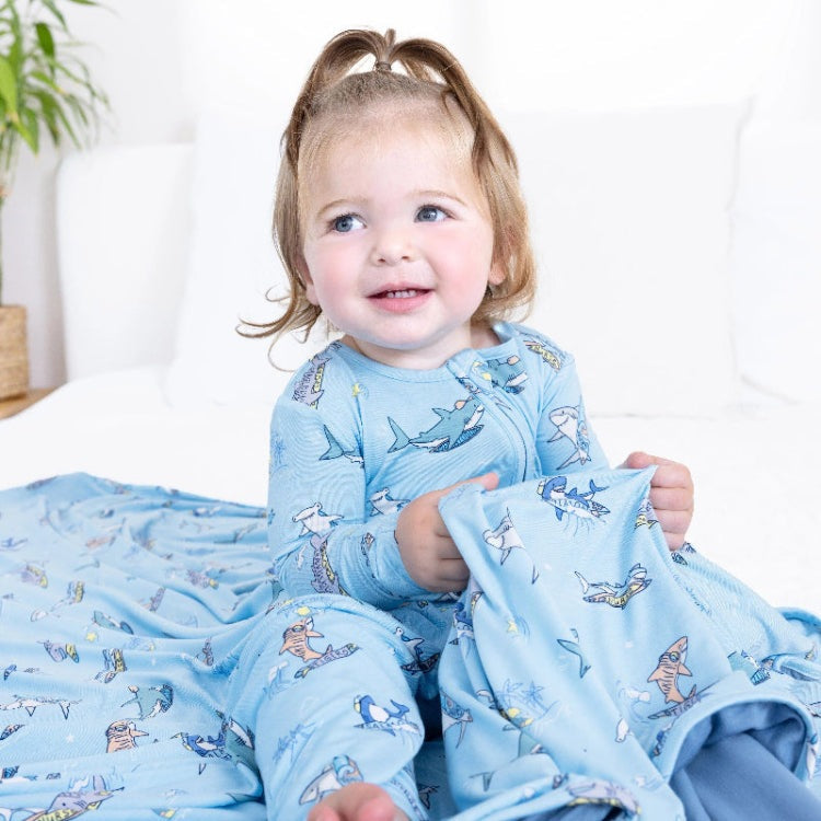 Bellabu Bear Bamboo Convertible Footie Shark School: toddler in blue shark-print footed pajamas sits on a bed, holding a blanket