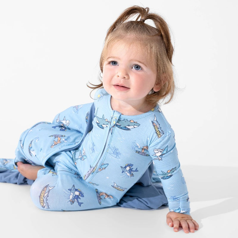 Bellabu Bear Bamboo Convertible Footie Shark School worn by a toddler sitting on white in a blue shark-print sleepsuit with front zipper.