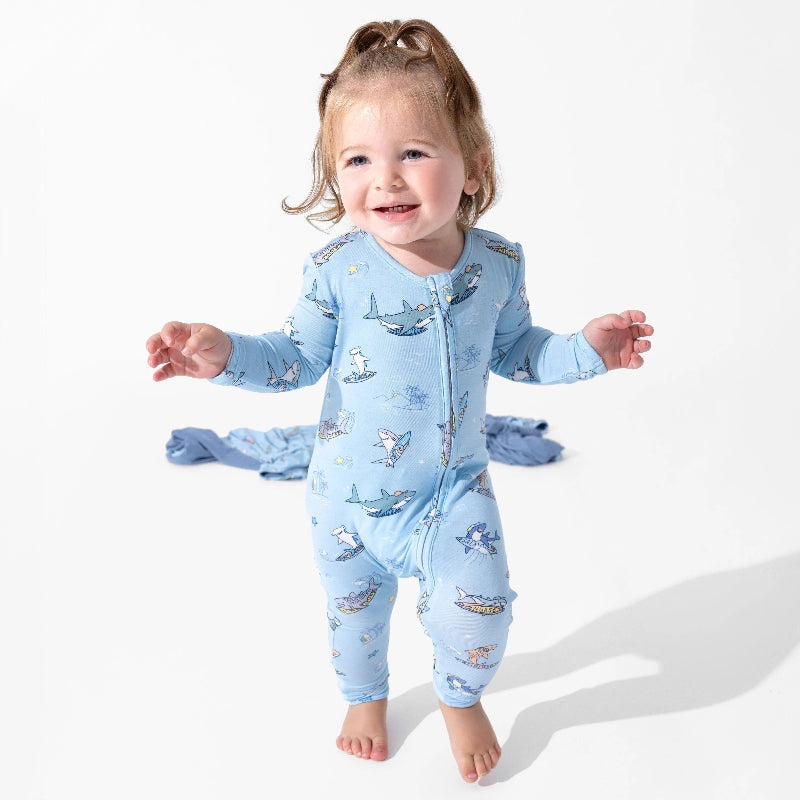 Bellabu Bear Bamboo Convertible Footie Shark School in light blue; baby stands smiling in the zipped, shark-print sleepwear.