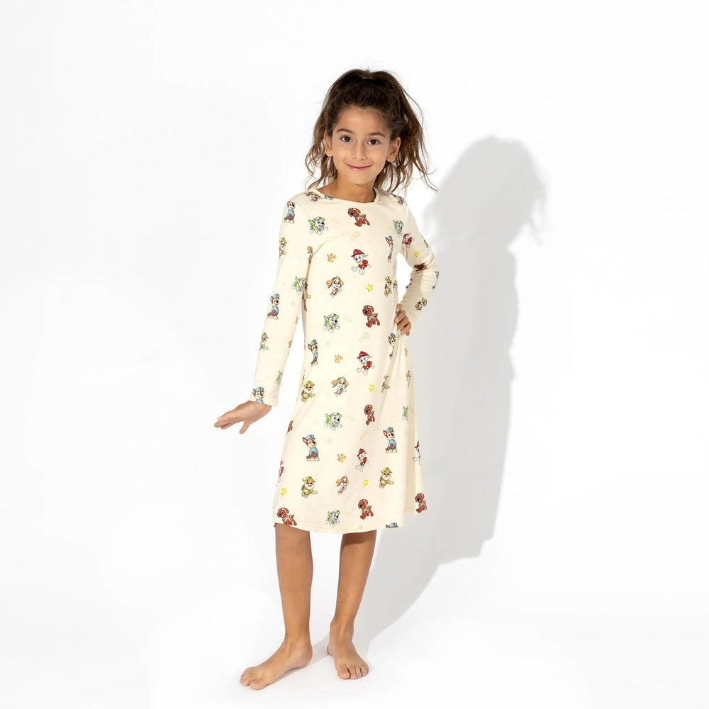 Bellabu Bear Bamboo Girls' Long Sleeve Dress Paw Patrol, cream with colorful print, girl poses with hand on hip.