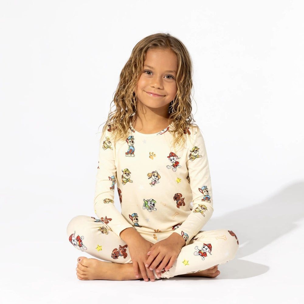 Bellabu Bear Bamboo Kids Pajamas Paw Patrol, cream bamboo fabric as a girl sits cross-legged showing cheerful Paw Patrol prints.