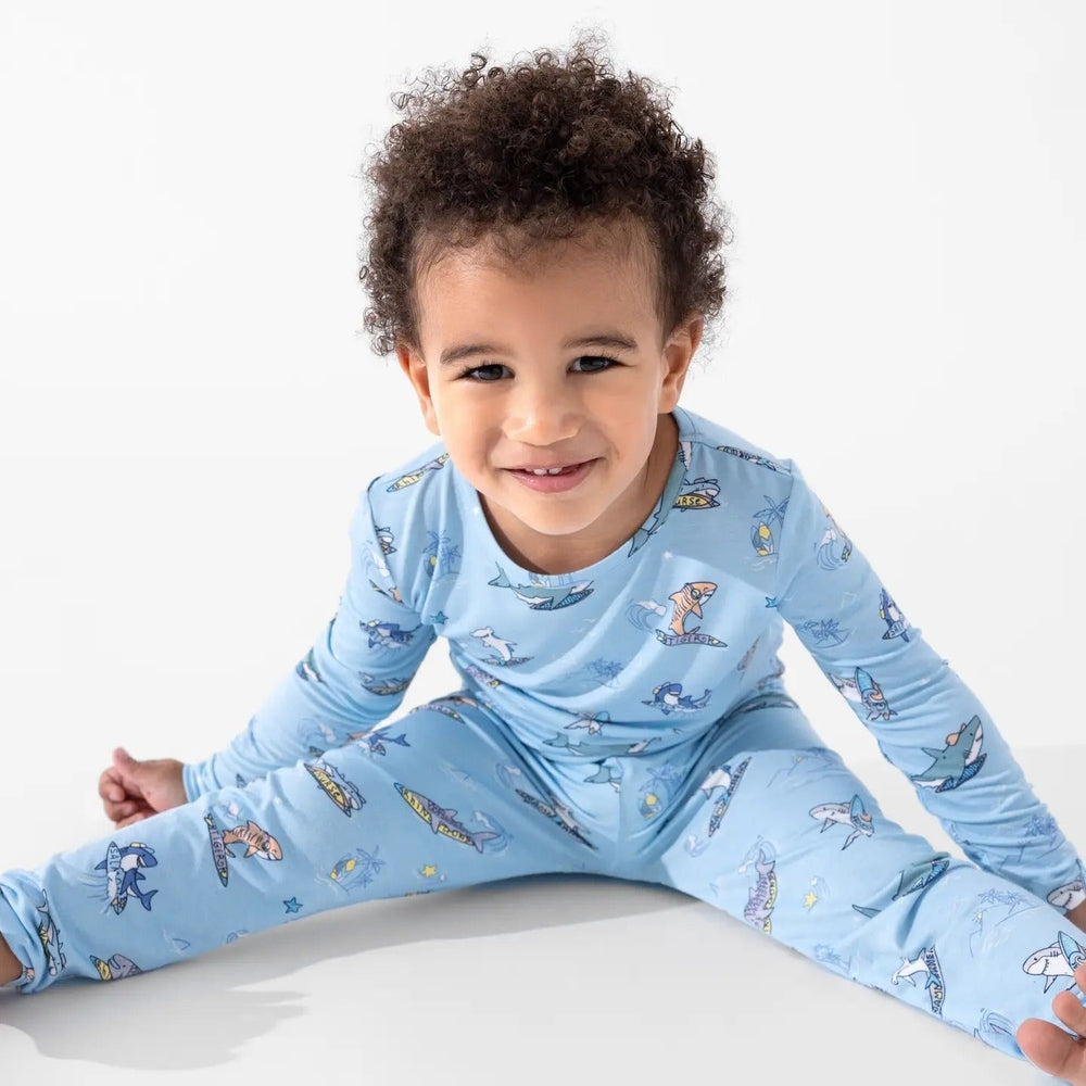 Bellabu Bear Bamboo Kids Pajamas Shark School blue set; smiling toddler sits cross-legged, highlighting soft bamboo fabric.