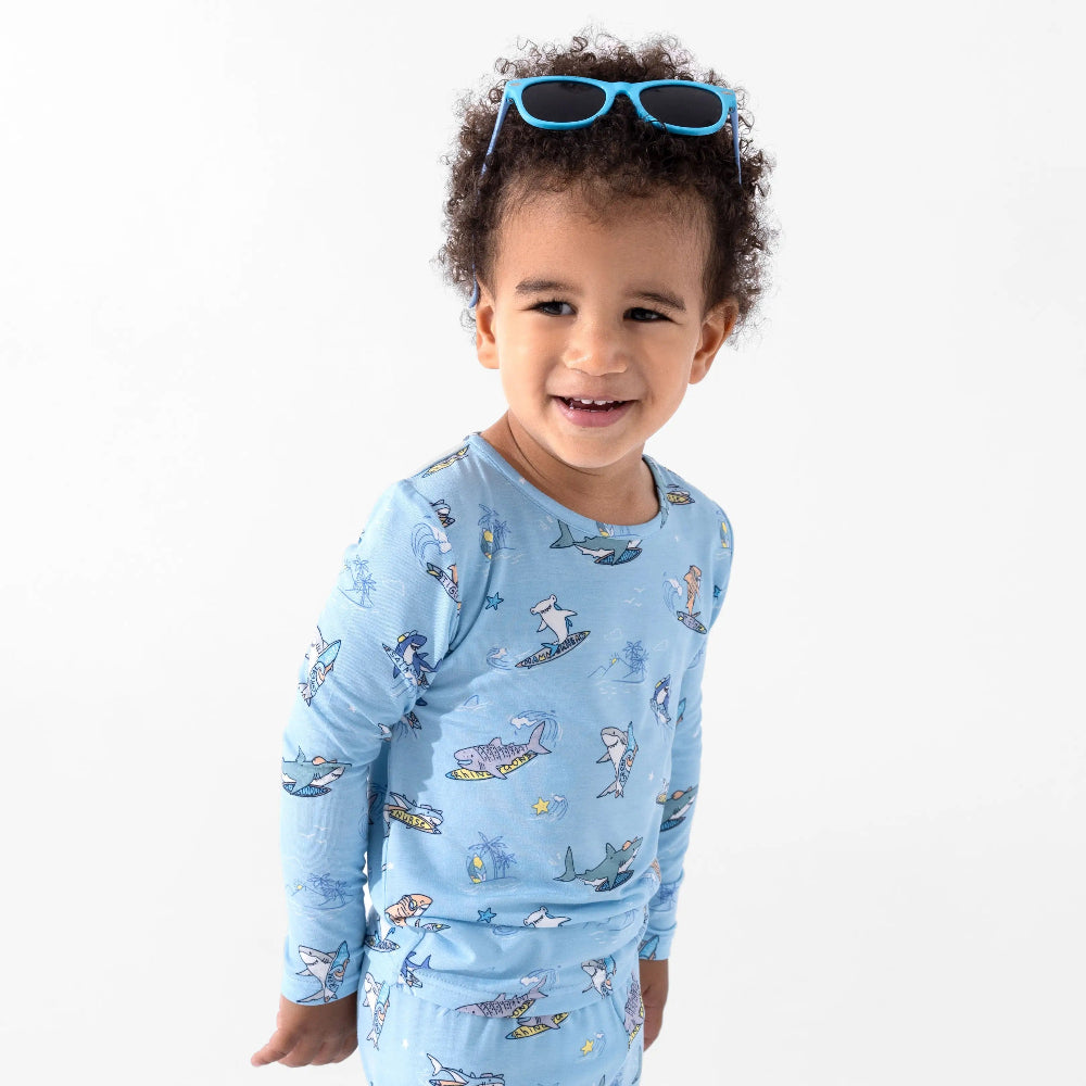 Bellabu Bear Bamboo Kids Pajamas Shark School set worn by a smiling toddler in blue shark-print sleepwear with sunglasses on head.