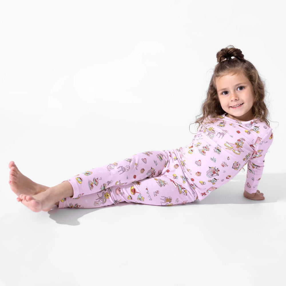 Bellabu Bear Bamboo Kids Pajamas Tea Party in pink as a smiling girl lounges on the floor.