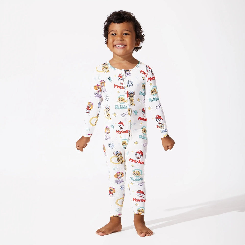 Toddler wearing Bellabu Bear Playful Pups Bamboo Convertible Footie Paw Patrol, white with colorful prints, smiling.