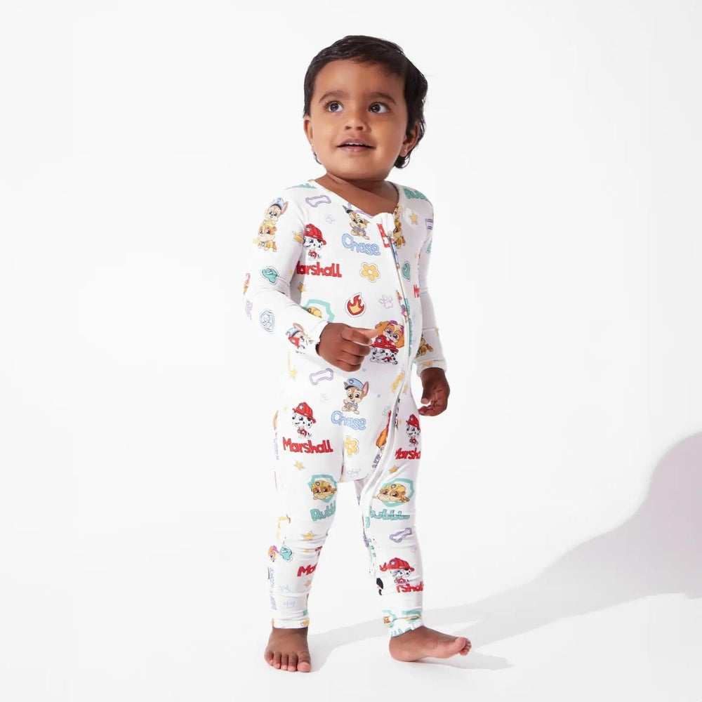 Bellabu Bear Playful Pups Bamboo Convertible Footie Paw Patrol; toddler stands in white sleepwear with colorful Paw Patrol prints and a visible front zipper.