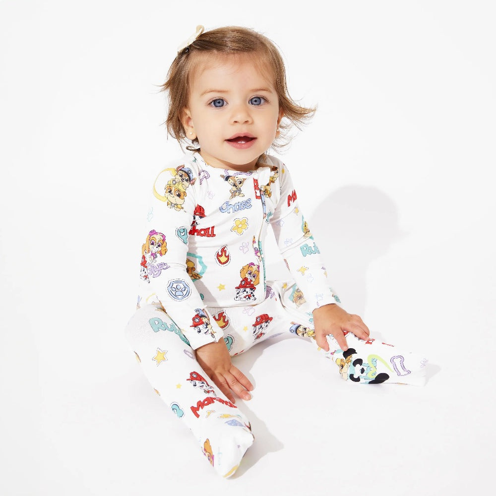 Baby in Bellabu Bear Playful Pups Bamboo Convertible Footie Paw Patrol, white with colorful prints, sitting on white.