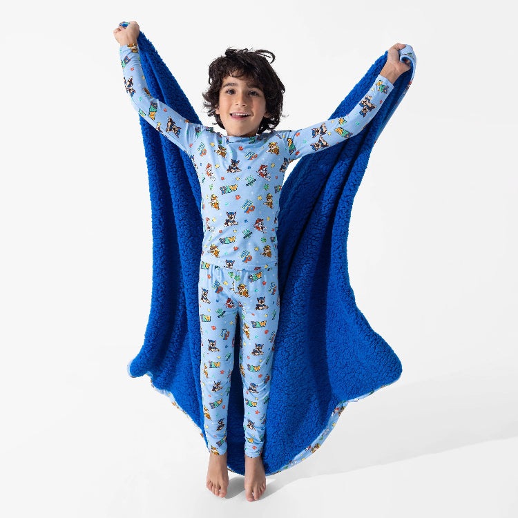 Bellabu Bear Varsity Blue Bamboo Kids Pajamas Paw Patrol; cheerful child wears soft bamboo PJs with Paw Patrol print, lifting a royal blue plush cape.