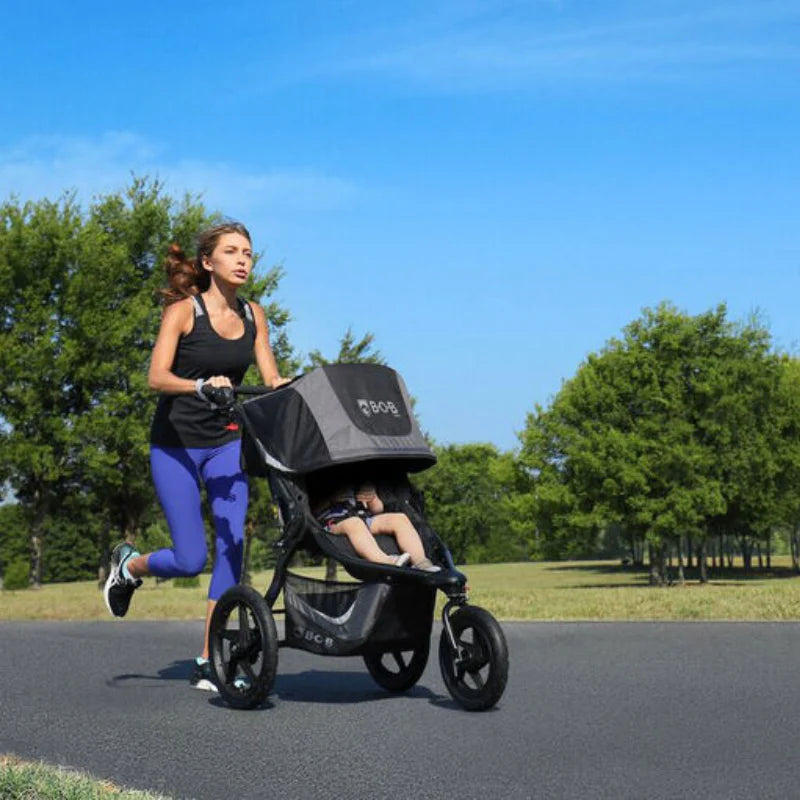 Bob Revolution Flex 3.0 Jogging Stroller in black/gray, parent jogging on a road with child seated.