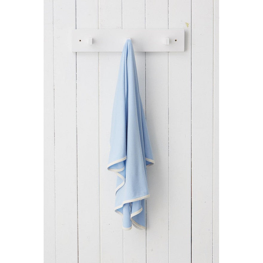 Boody Wear Stretch Blanket Sky baby blanket in light blue with white trim, draped from a white rack on a paneled wall.