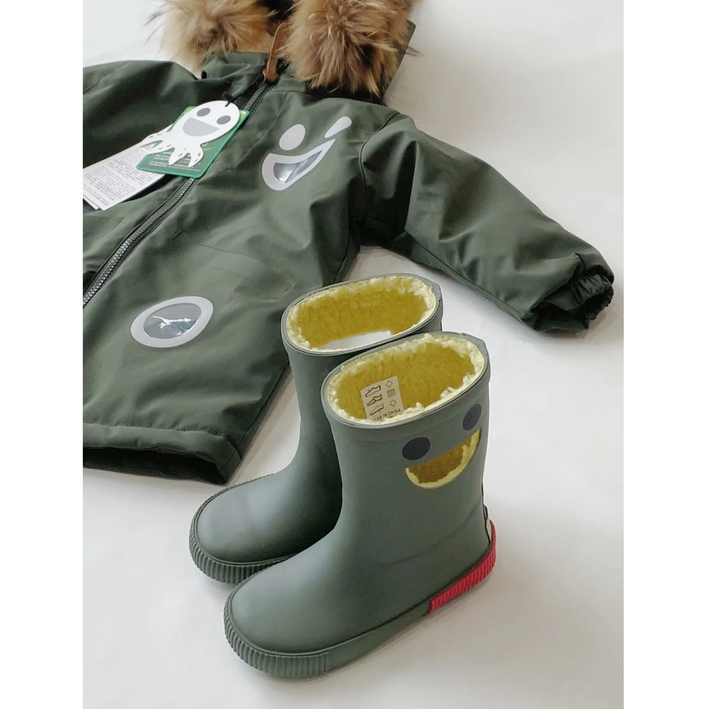 Boxbo Wistiti fleece-lined rainboots in forest green with yellow interior and smiley face cutouts, standing beside a green jacket.