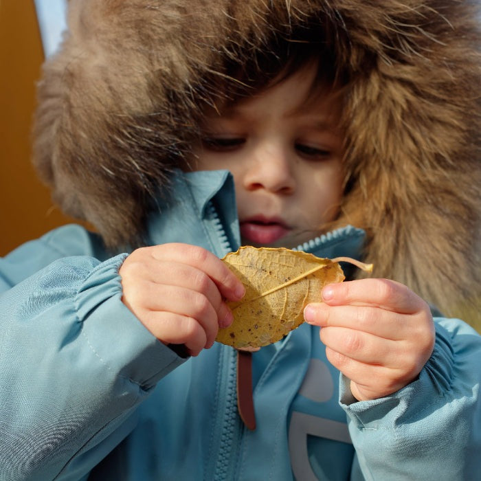 Boxbo Wistiti fleece-lined waterproof snowproof fur jacket blue; toddler in fur-hooded coat examines a leaf.