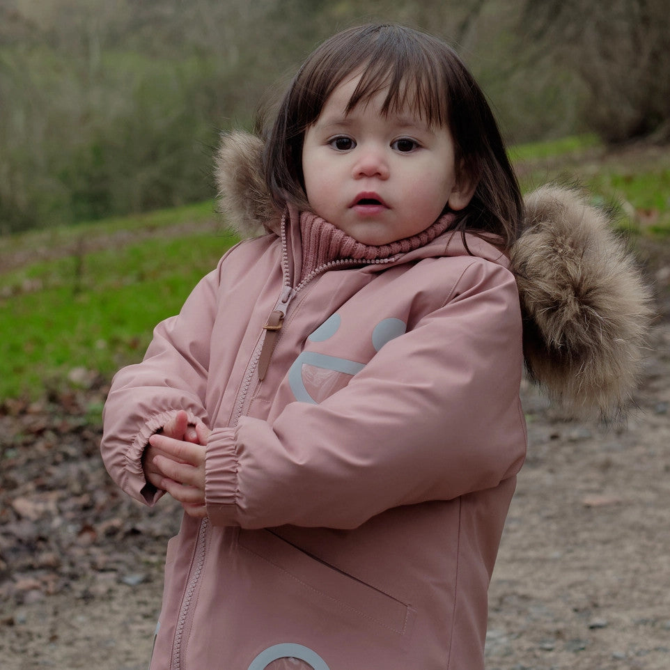 Boxbo Wistiti fleece-lined waterproof fur jacket in dusty rose pink, worn by a toddler outdoors with fur-trim hood.