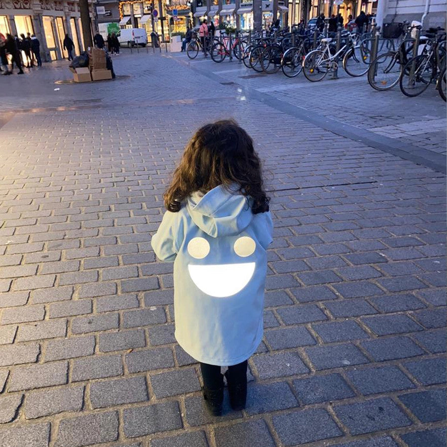 Boxbo Wistiti blue fleece-lined waterproof jacket on a child walking on cobblestone street with a big white back smile.