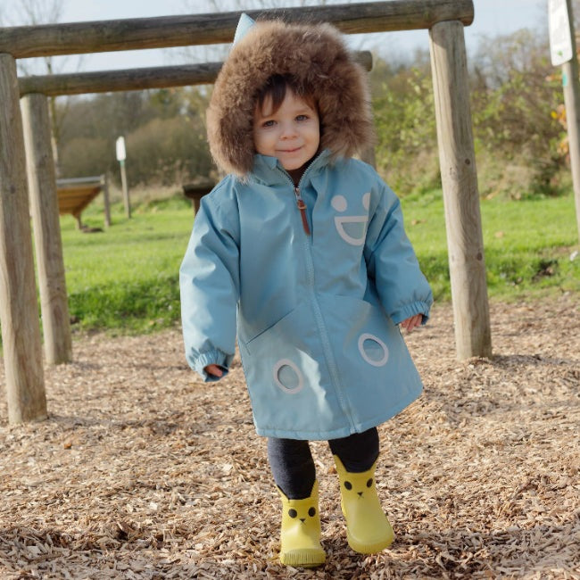 Boxbo Wistiti fleece-lined waterproof jacket blue; toddler in fur-trimmed hood walks on wood chips in park.