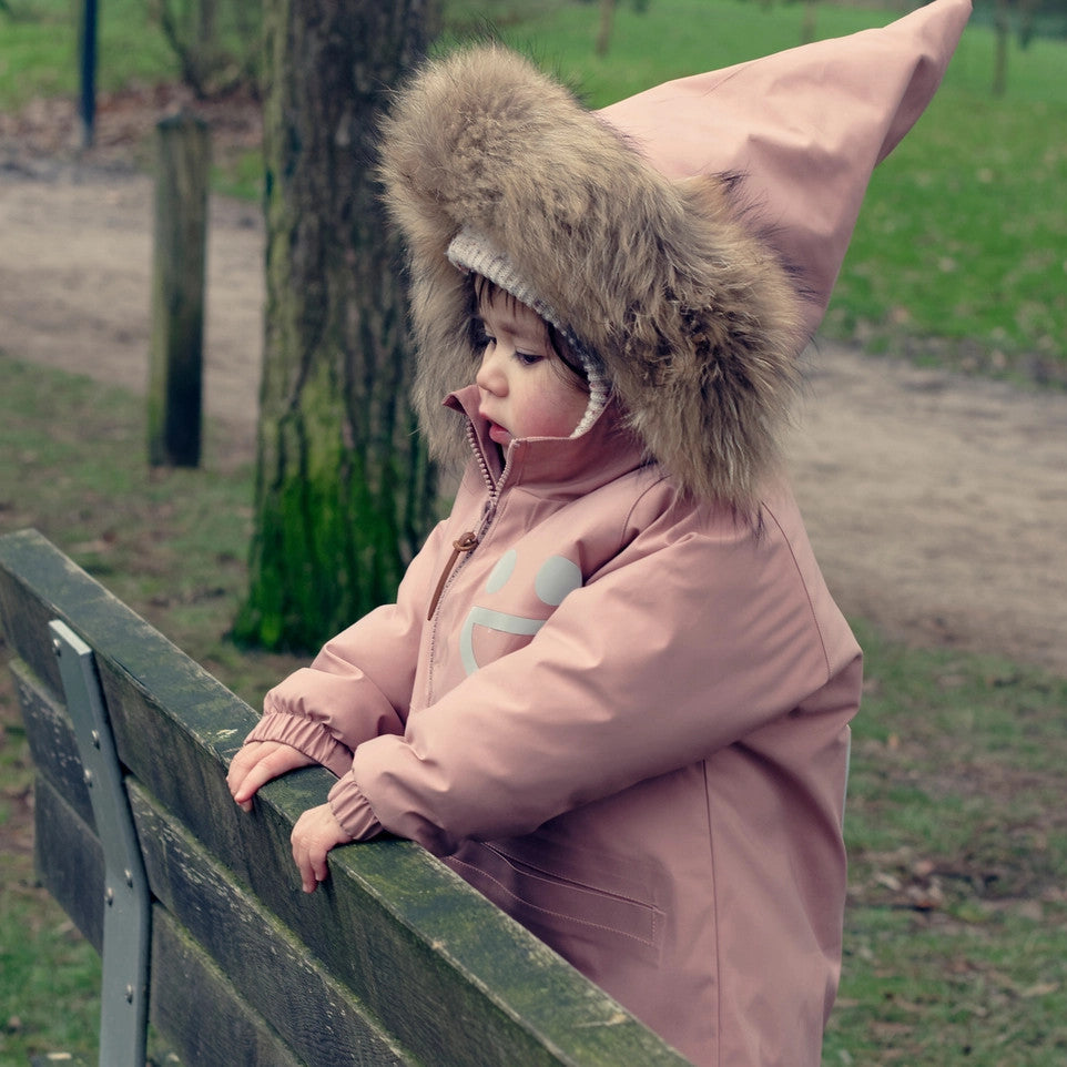 Boxbo Wistiti fleece-lined waterproof snowproof fur jacket in dusty rose pink, toddler leaning on a park railing with a fur-trim hood