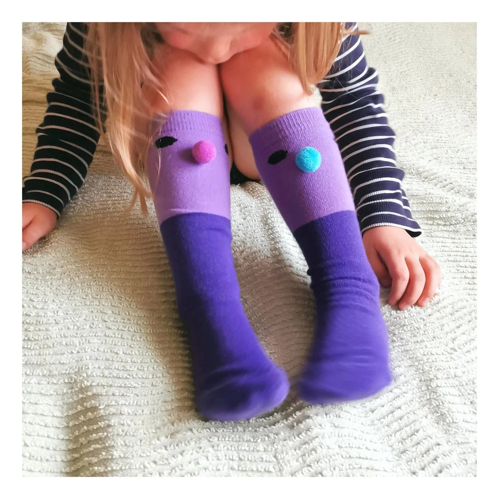 Boxbo Wistiti High Sock Violet on a child, purple knee-length socks with pink and blue pom-poms worn.