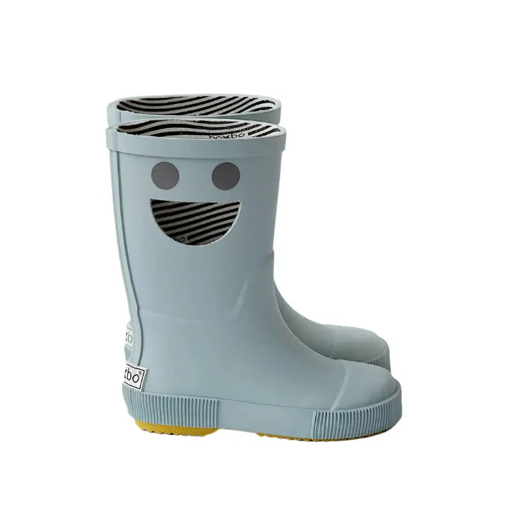 BOXBO Wistiti Rainboots Platine; light blue rubber kids' boots with a smiley face, striped lining, and yellow outsole, pair standing.