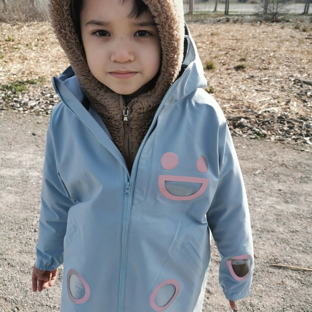 Boxbo Wistiti Windbreaker Rain Jacket Blue worn by a toddler outdoors, plush hood lining and pink smiley motif.