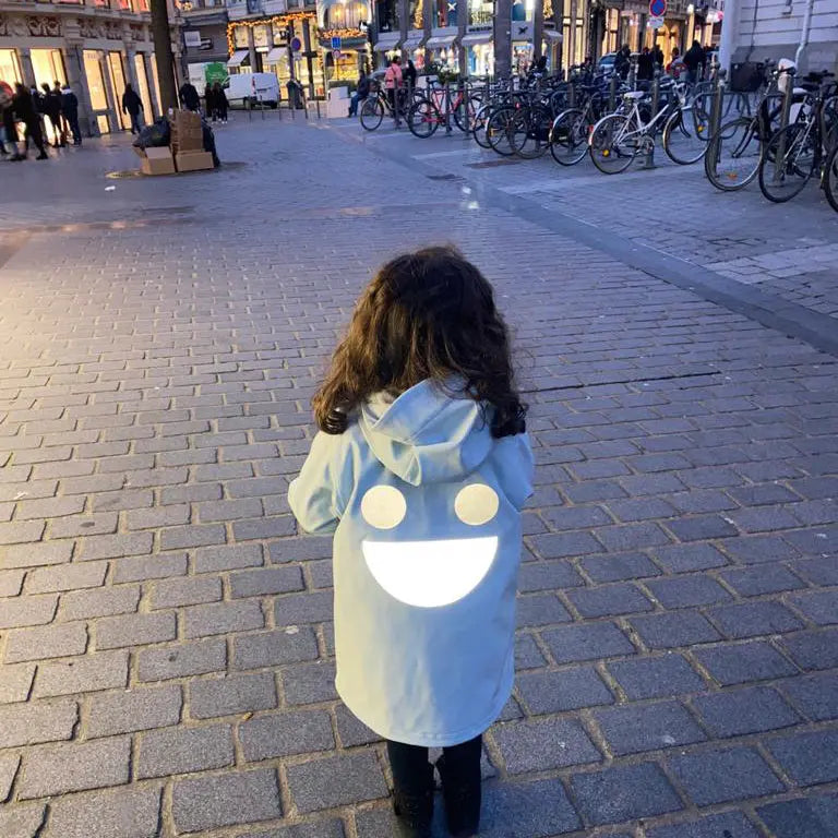 Boxbo Wistiti Windbreaker Rain Jacket Blue, hooded child walking on a city street at dusk with a large white back smile.