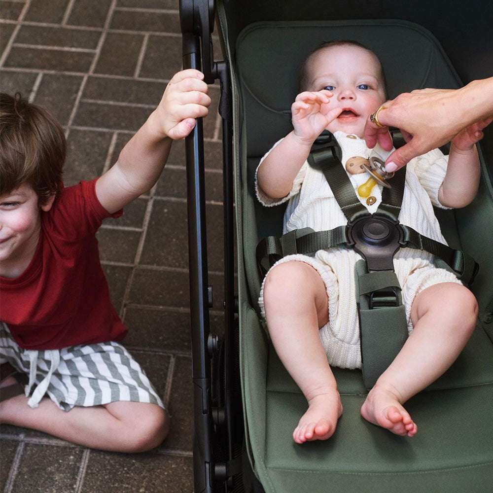 Bugaboo Butterfly 2 stroller in green; baby secured in harness while adult adjusts strap.