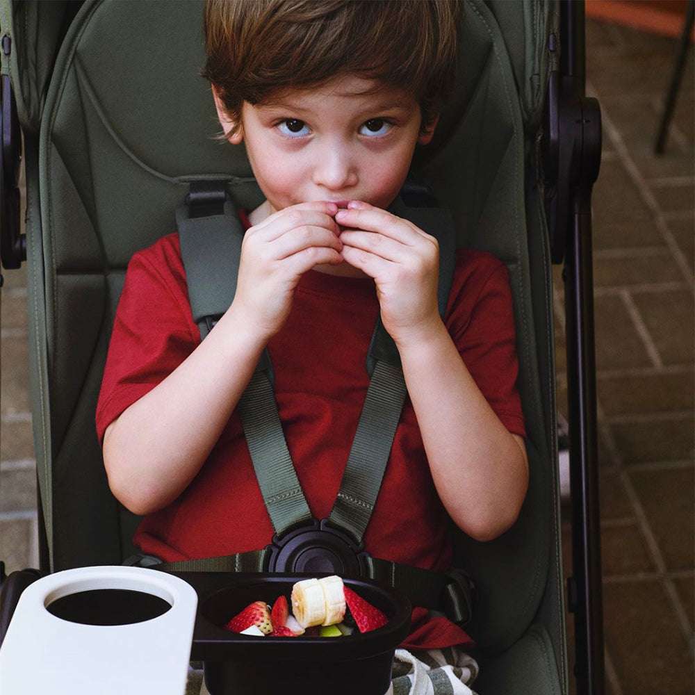 Bugaboo Butterfly 2 stroller; green seat, child in red shirt eating fruit snack.