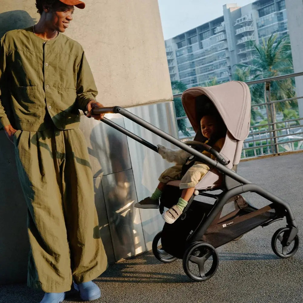 Bugaboo Dragonfly Stroller Complete with beige canopy and black frame, caregiver pushes a seated child.